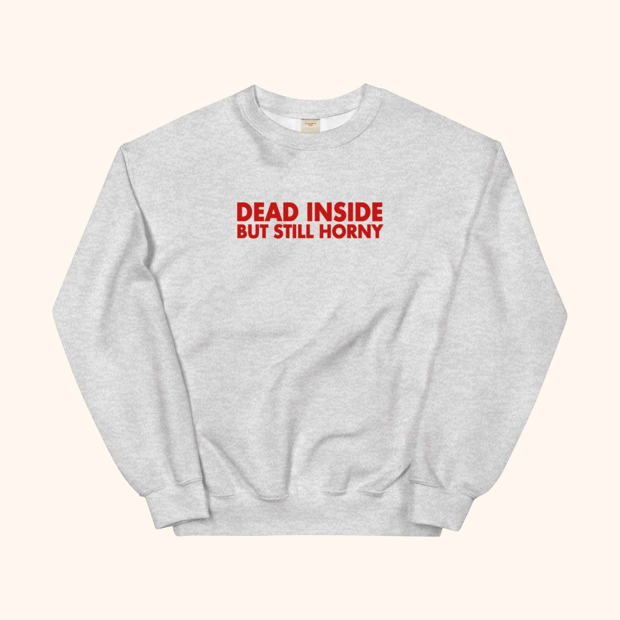 Gray sweatshirt with red “DEAD INSIDE BUT STILL HORNY” graphic on front