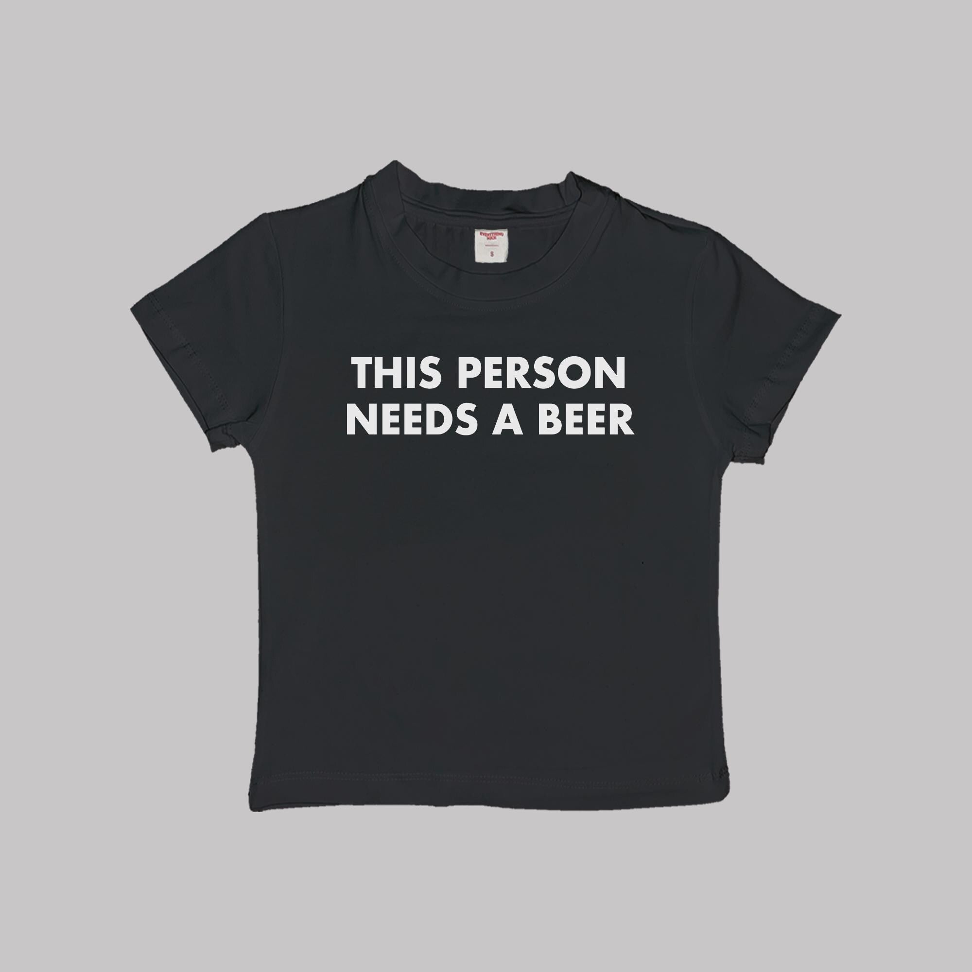 Black cropped baby tee with “THIS PERSON NEEDS A BEER” lettering