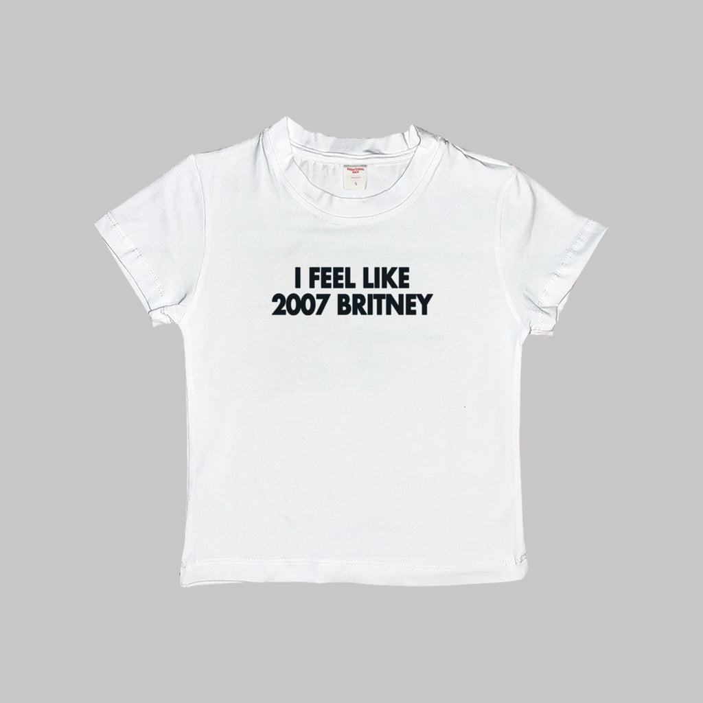 White baby tee crop top, crew neck, “I FEEL LIKE 2007 BRITNEY” printed text.