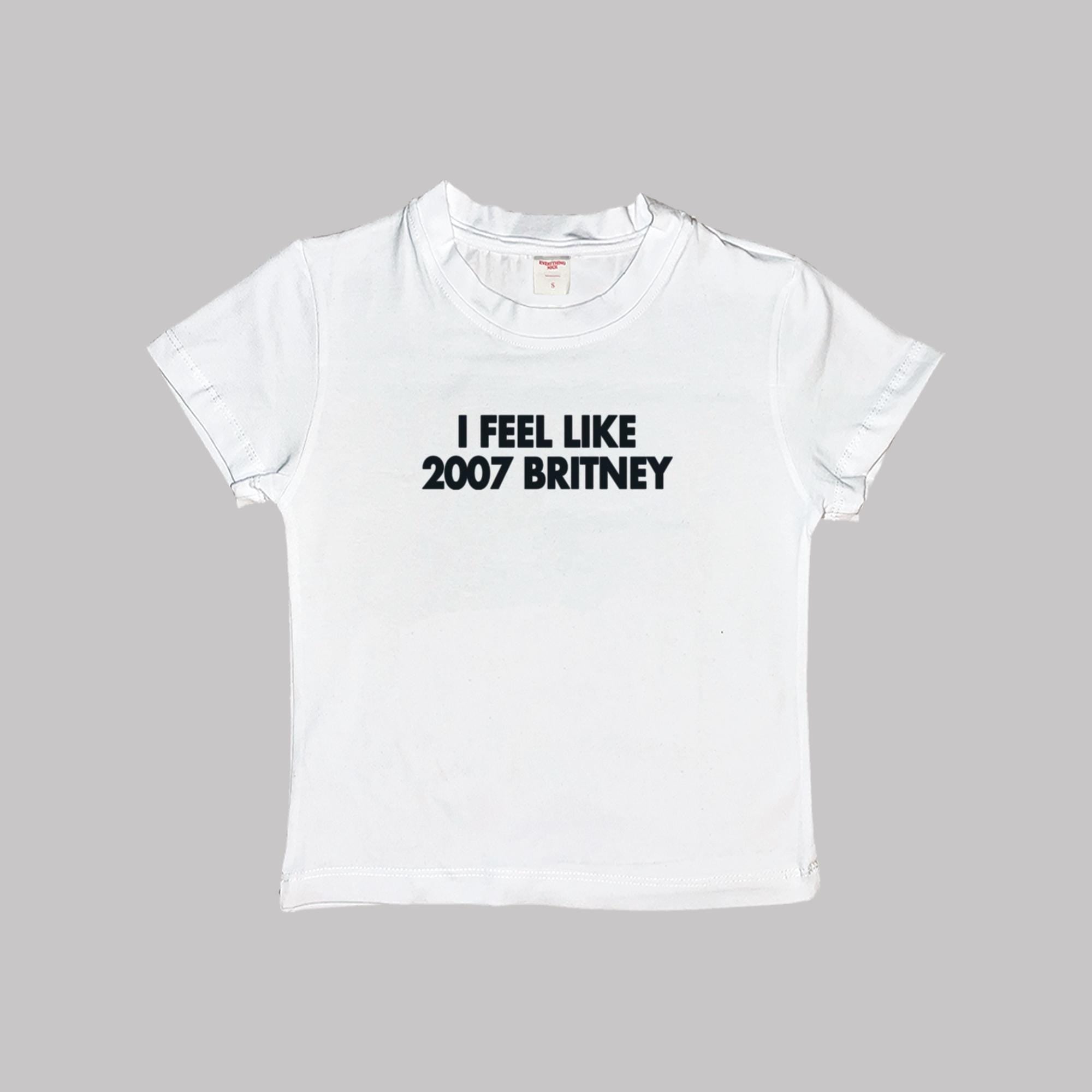 White baby tee crop top, crew neck, “I FEEL LIKE 2007 BRITNEY” printed text.