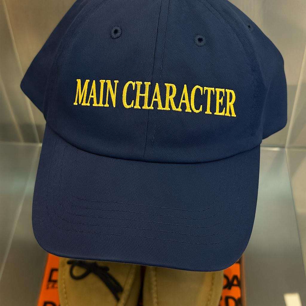 Navy baseball cap with yellow embroidered Main Character lettering