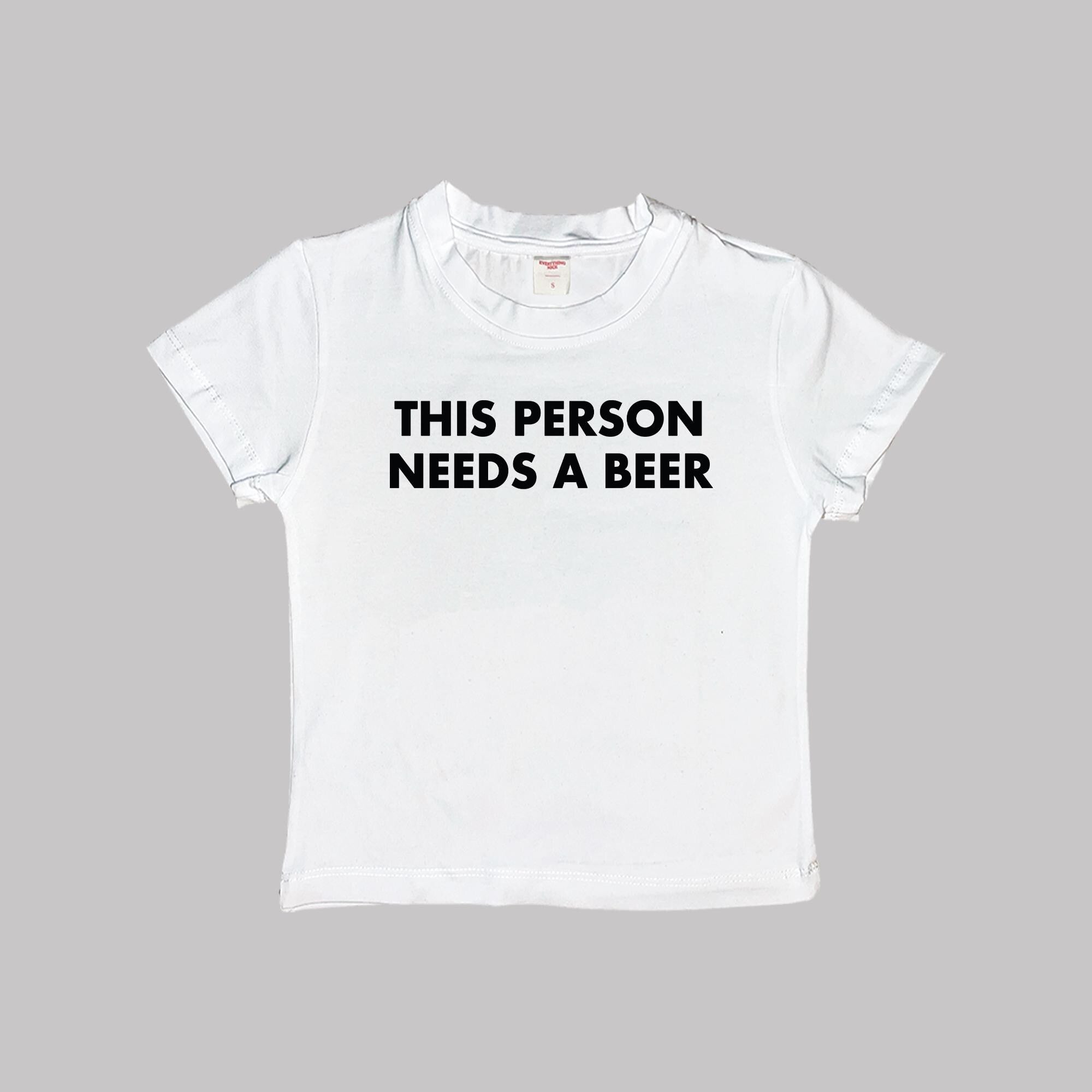 White cropped T-shirt, crew neck, “THIS PERSON NEEDS A BEER” front graphic