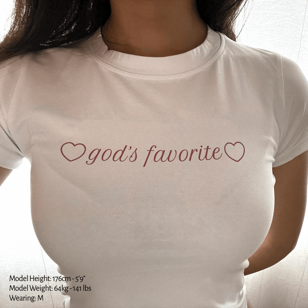 White baby tee with "god's favorite" heart text graphic on crew neck chest