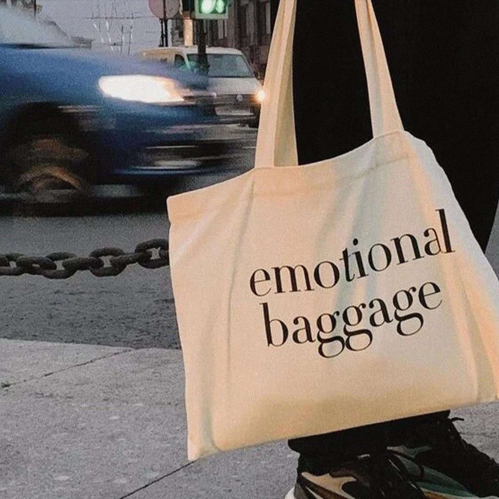 Beige tote bag with long handles, printed text “emotional baggage” on the front.