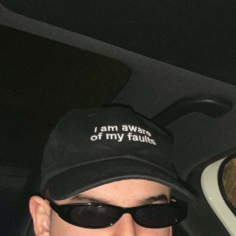Black hat with 'I am aware of my faults' text and curved brim