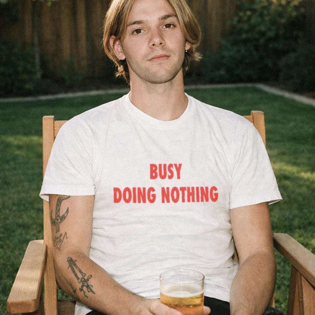 White unisex T-shirt with red "BUSY DOING NOTHING" graphic on front