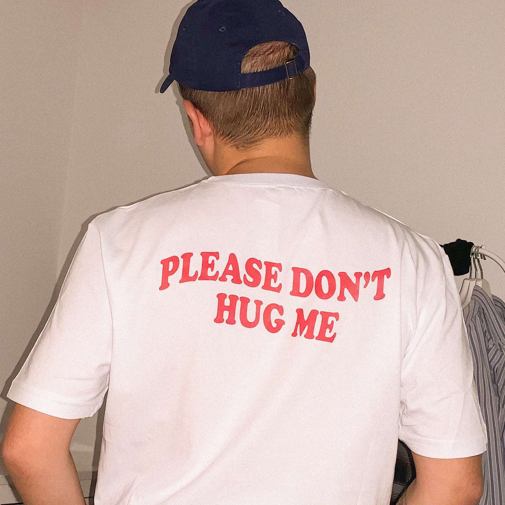 White graphic T-shirt with red “PLEASE DON’T HUG ME” text on the back